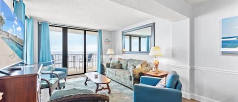 A room with a balcony, a sofa, a chair, a table, and a lamp.