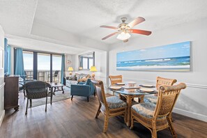 A spacious living area with a dining table, wicker chairs, and a ceiling fan.