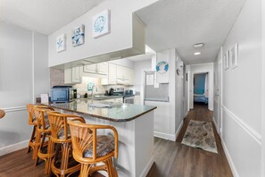 A modern kitchen with white cabinetry, a central island, and a dining area with wicker chairs.