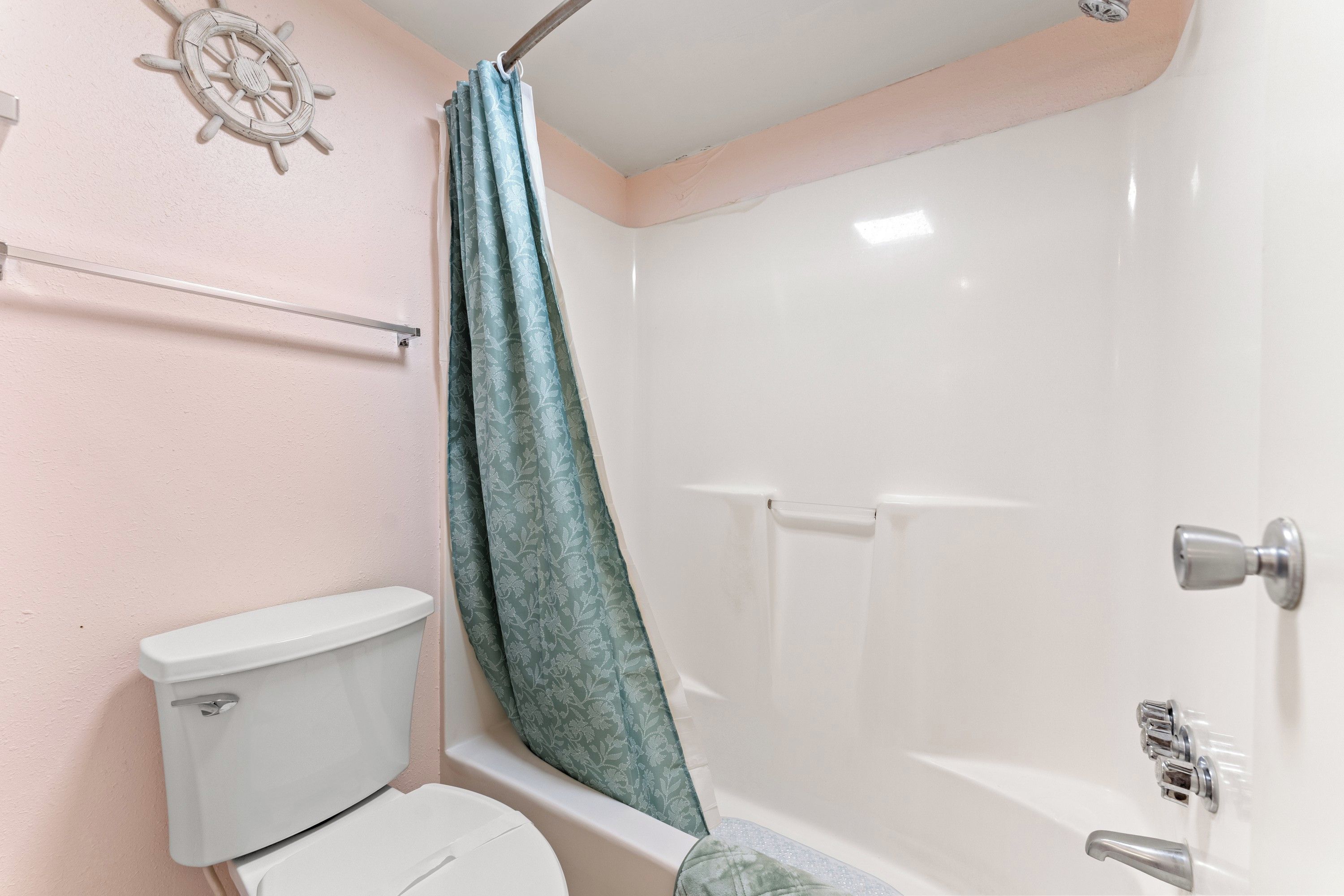 Un baño con inodoro, ducha y un adorno de timón de barco montado en la pared.