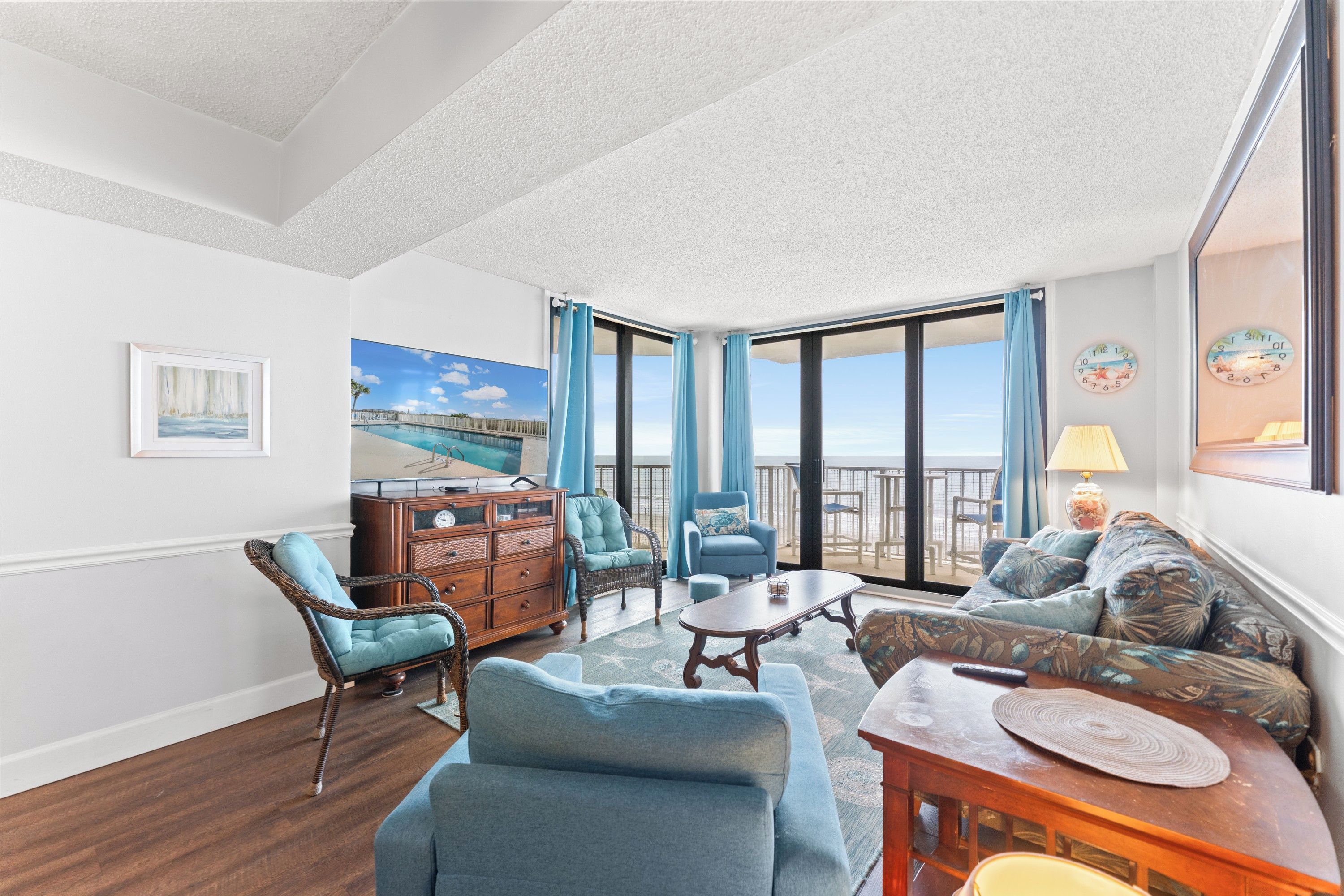 A room with a view of the sea, a wooden cabinet, a wicker chair, a blue sofa, and a table.