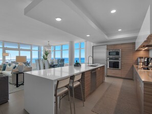 A modern kitchen with a central island, built-in appliances, and large windows offering ocean views.
