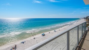 Vista a la playa desde un balcón, con cielo despejado, arena y algunas personas.