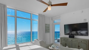 Una habitación de hotel con una cama grande, televisión, ventilador de techo y vista al océano.