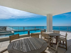 A rooftop pool area with a view of the ocean, a pool, and seating arrangements.