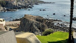 A coastal view with rocky terrain, a palm tree, and a building with a balcony overlooking the sea. - Top Floor Large 2 Bedroom  Ocean/Beach Views Vaulted Ceiling Lots of Windows (Cabo San Lucas)