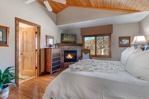 Une chambre avec une cheminée, un plafond en bois et un lit recouvert de linge de lit blanc.