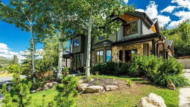 A two-story house with a stone facade, large windows, and a well-maintained garden with rocks and shrubs.