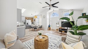 Een moderne woonkamer met een bank, salontafel en een televisie. Achtergrond is een keuken met een eethoek.
