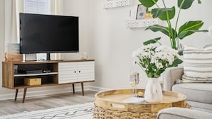Een moderne woonkamer met een flatscreen televisie, een houten tv-meubel, een rieten salontafel met een bloevas en een grote plant.