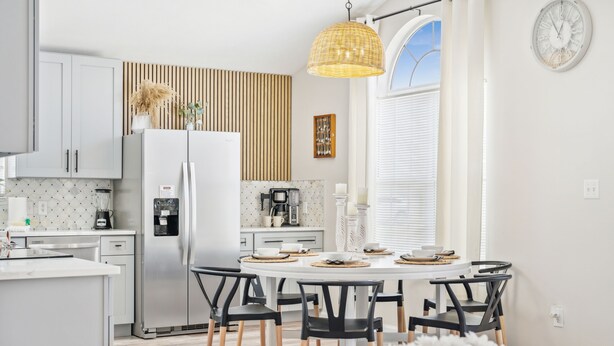 Een moderne keuken met witte kasten, een centraal eiland en een eethoek met zwarte stoelen.