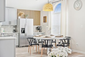 Une cuisine moderne avec des meubles blancs, un îlot central et un coin repas doté de chaises noires.