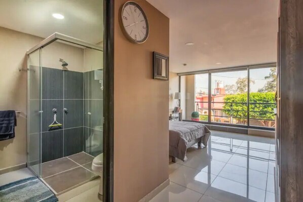 A modern bathroom with a glass-enclosed shower, a visible toilet, and a large window offering a view of the outdoors.
