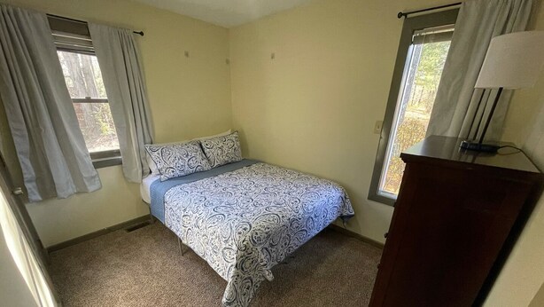 Ein Schlafzimmer mit einem Bett, zwei fensterbepflanzten Fenstern, einem Schminktisch und Teppichboden.