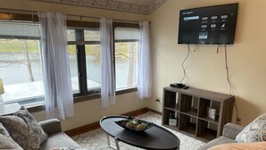 Ein Wohnzimmer mit einem an der Wand montierten Flachbildfernseher, einem Couchtisch mit Dekoration und einem Sofa mit gemusterten Kissen.