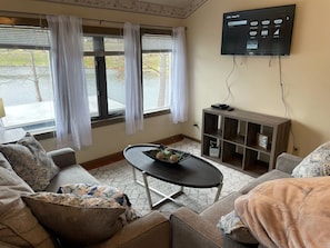 Een woonkamer met een flatscreen televisie aan de muur, een salontafel met decoratieve objecten en een bank met patroon kussens.