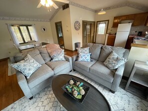A living room with two grey sofas, a coffee table with decorative items, and a kitchen in the background.