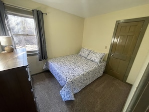 Un dormitorio pequeño con cama, cómoda, ventana con cortinas y puerta.