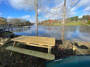 Une table de pique-nique et des bancs au bord d’un lac, avec une jetée et un bateau en arrière-plan.