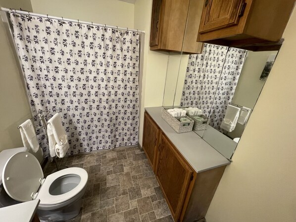 Een badkamer met douchegordijn, toilet, wastafel met spiegel en houten kastjes.