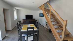 Una sala moderna con una mesa de comedor, sillas, un televisor y una escalera de madera.