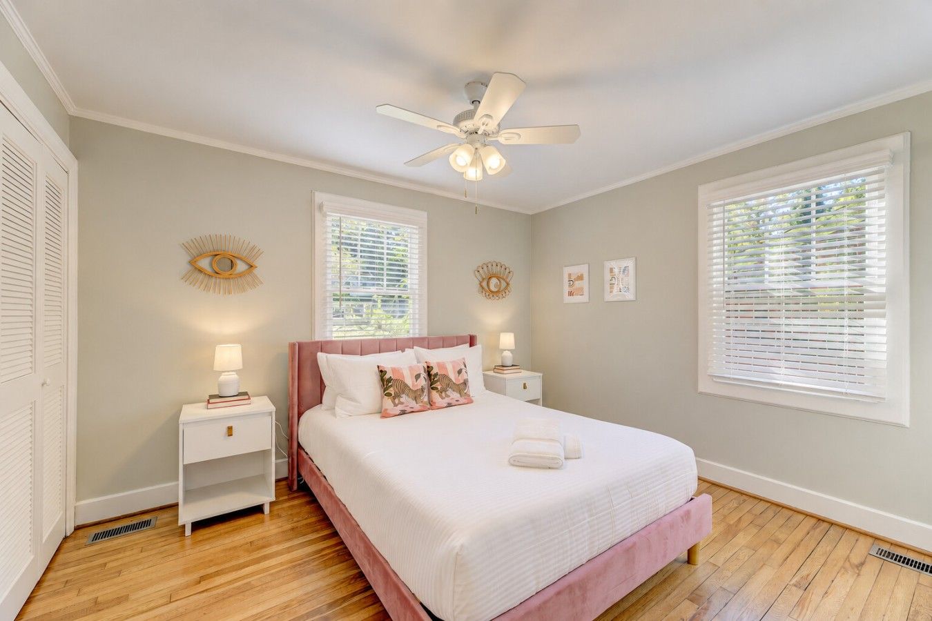A bedroom with a bed, two bedside tables, a ceiling fan, and two windows with blinds.