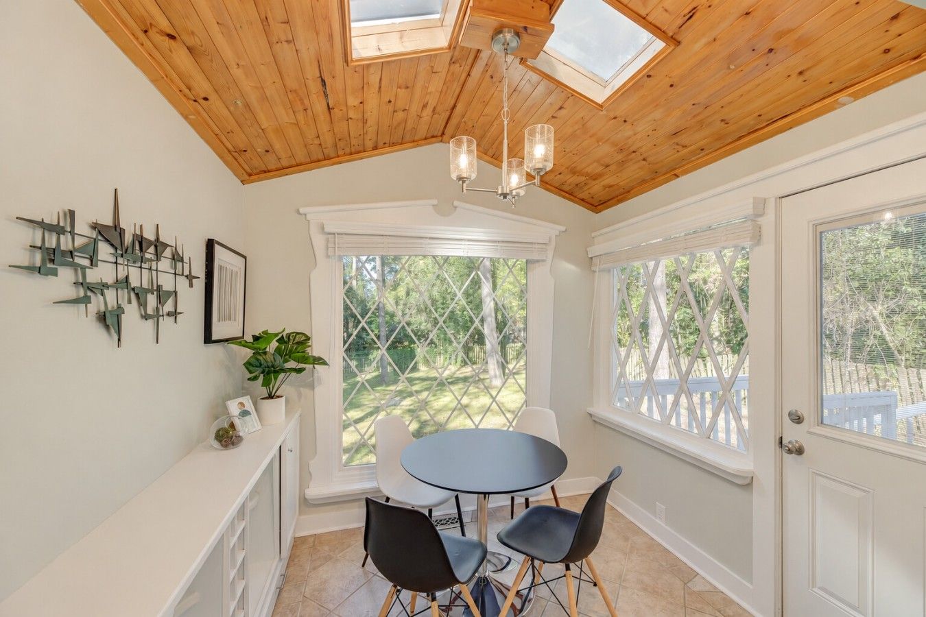 A dining area with a round table and chairs, a chandelier, and a view of the outdoors through large windows.