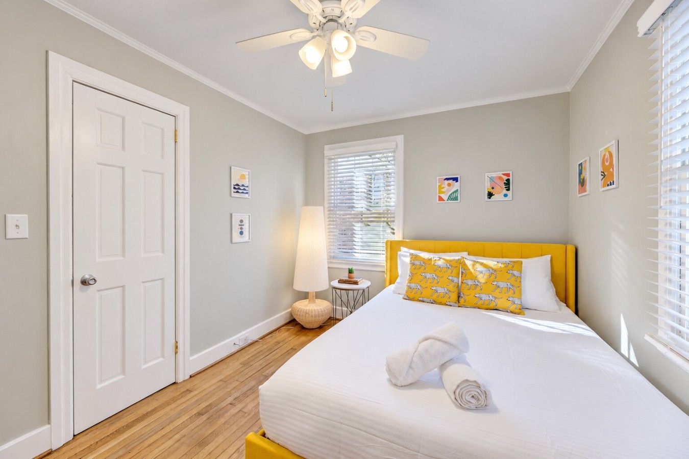 A bedroom with a bed, a ceiling fan, a bedside table, and a window with blinds.
