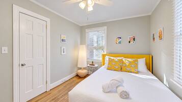 A bedroom with a bed, a ceiling fan, a bedside table, and a window with blinds.