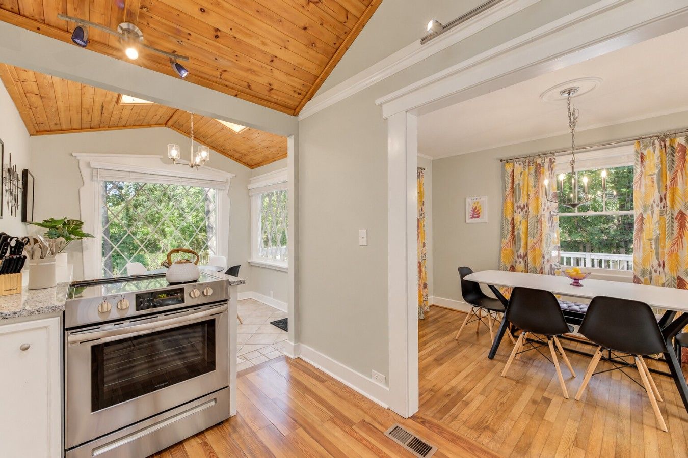 A kitchen with a modern stove, a dining area with a table and chairs, and a view of greenery outside.