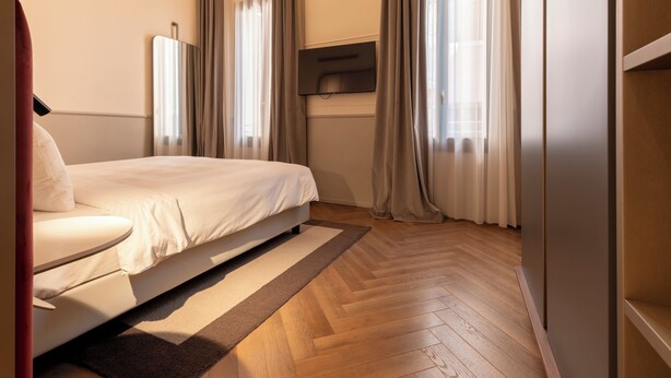 A modern hotel room with a bed, a TV mounted on the wall, and a wooden floor.