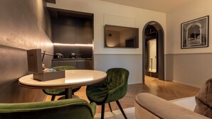 A modern kitchen with a round dining table and green chairs, a small seating area with a sofa, and a framed picture on the wall.