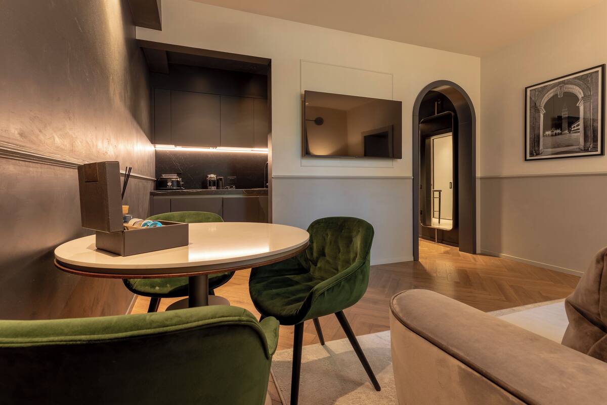 Een moderne keuken met een ronde eettafel en groene stoelen, een zithoek met een bank en een lijst met een afbeelding aan de muur.