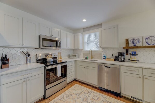 A modern kitchen with white cabinets, stainless steel appliances, and a patterned rug.