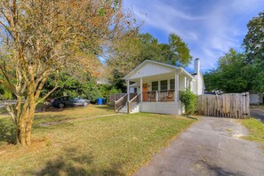 A small, single-story house with a porch, a fenced yard, and a car parked outside.