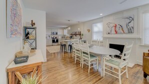 A spacious kitchen with white cabinets, a central island, and a dining area with white chairs and a round table.