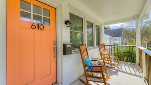 A porch with a bright orange door marked with the number 610, wooden rocking chairs, and a white railing.