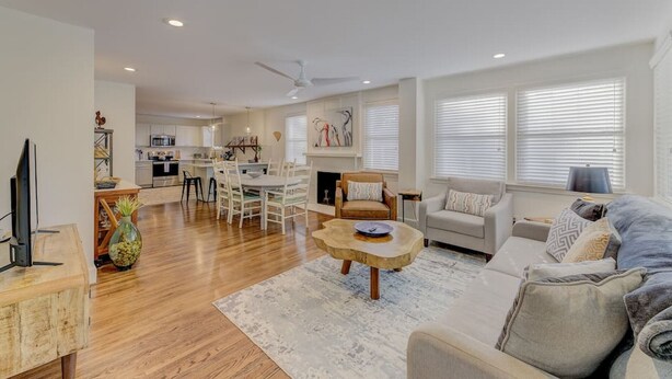 A spacious living area with a sofa, coffee table, and a dining table with chairs. There is a fireplace and a kitchen in the background.