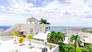 A resort with a rooftop terrace, palm trees, and a view of the ocean.