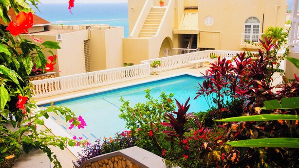 A pool area with a view of the ocean, a white staircase, and a gazebo.
