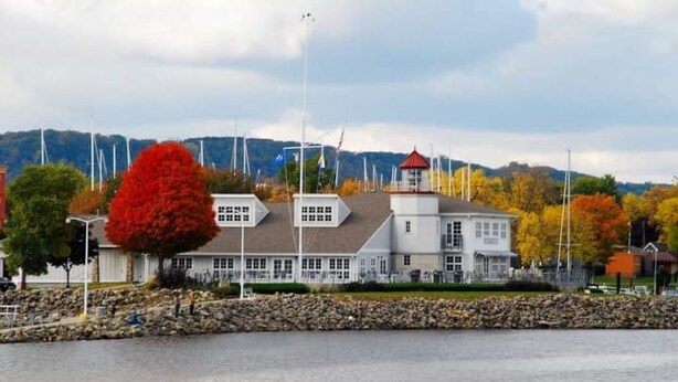Un edificio frente al mar con un árbol rojo destacado, un faro y un litoral rocoso.