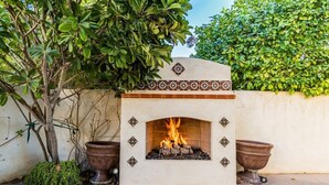 Una chimenea de piedra con fuego, rodeada de azulejos decorativos y plantas en macetas.