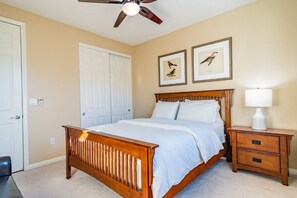 A bedroom with a wooden bed, a nightstand, a ceiling fan, and two framed bird pictures on the wall.