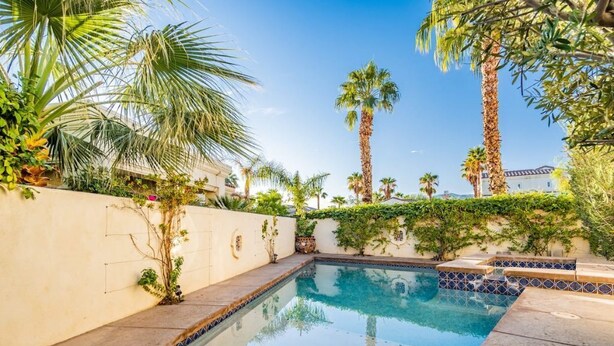 Una piscina rodeada de palmeras y vegetación, con un cielo azul despejado.