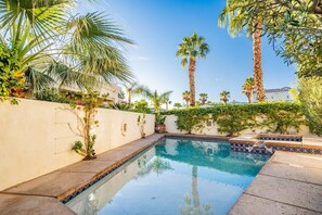 Una piscina envoltada de palmeres i vegetació, amb un cel blau i clar.