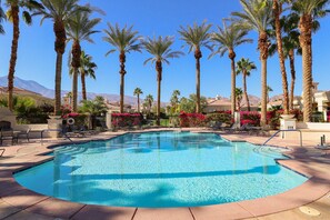 A swimming pool with palm trees and a mountain backdrop.