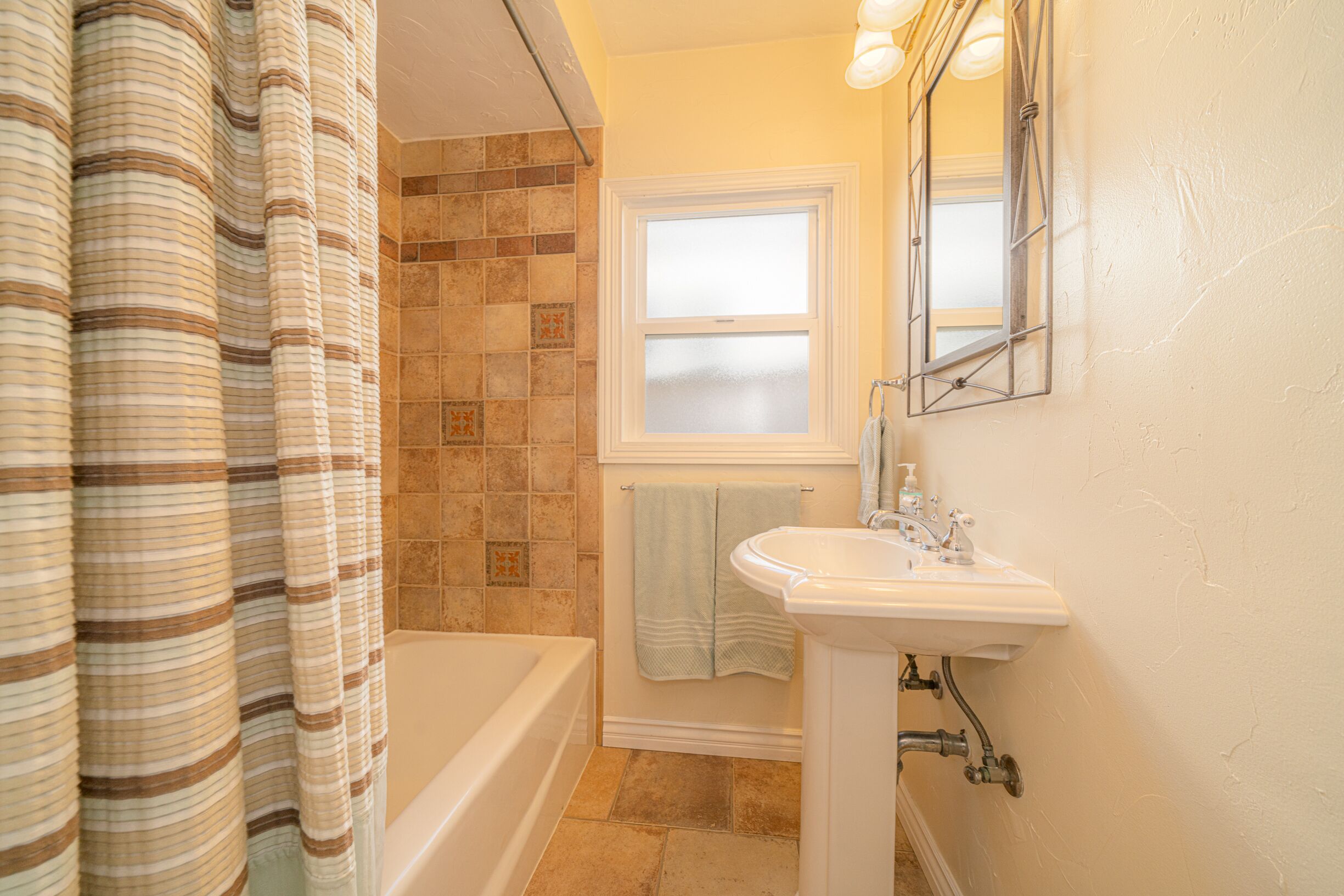 A bathroom with a bathtub, a sink, and a window with frosted glass.