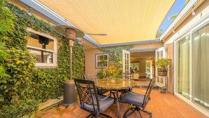An outdoor patio with a round table and chairs, surrounded by lush greenery and potted plants.