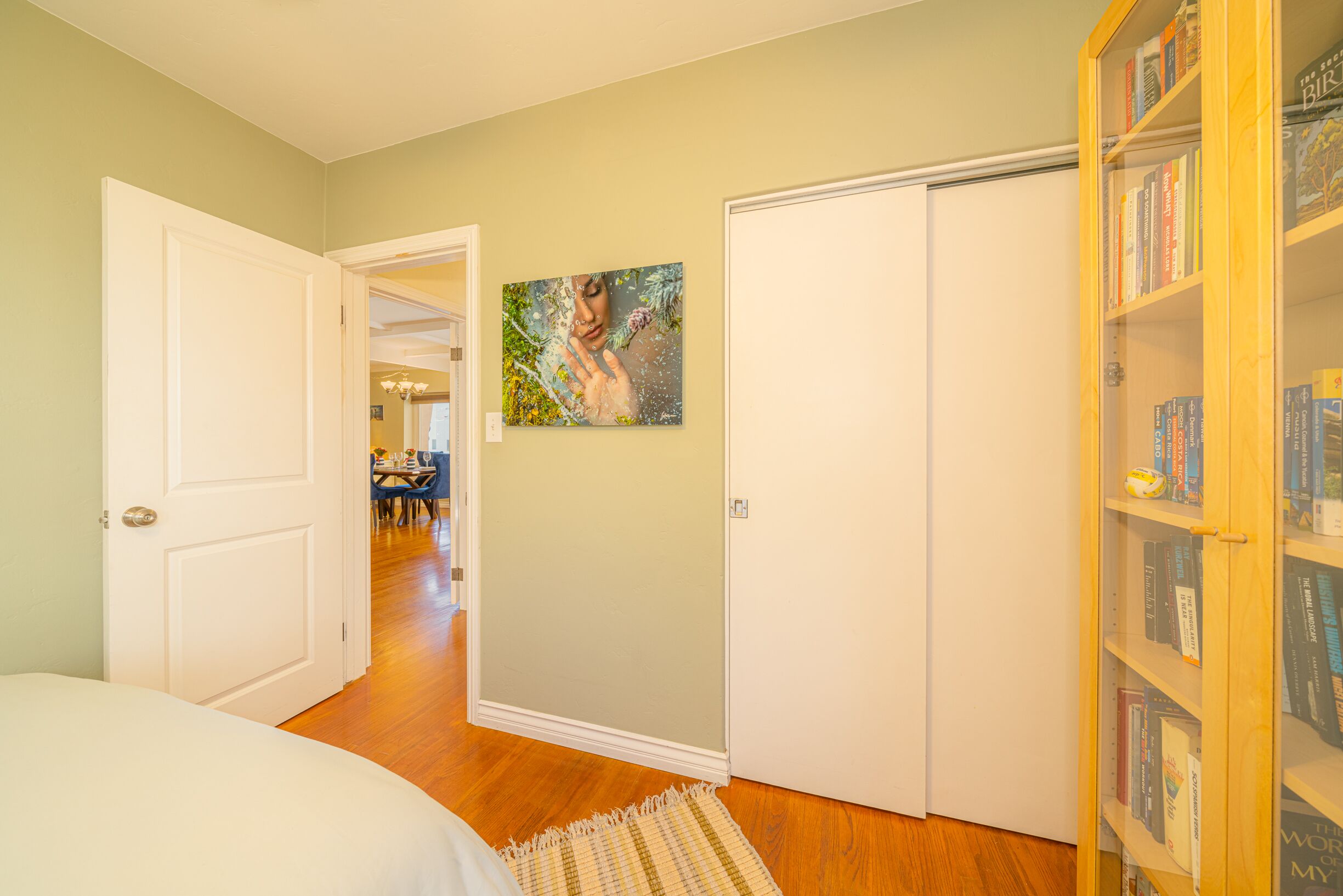 A bedroom with a bed, a wardrobe, a bookshelf, and a painting on the wall.