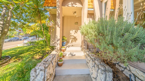 A house with a stone pathway leading to the front door, surrounded by potted plants and greenery.